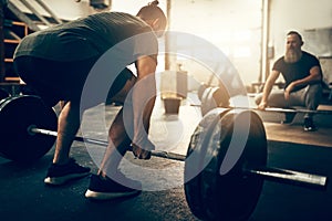 Fit young man lifting heavy weights with a gym partner