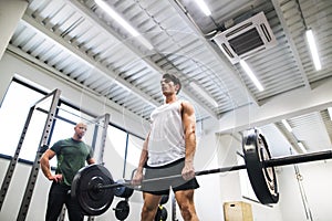 Fit young man with a personal trainer in gym working out, lifting barbell.