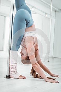 Fit young pole-dancer stretching near the pole.