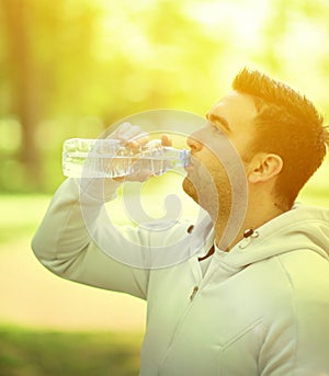Fit young sportsman drinking water from plastic bottle after workout in outdoor park