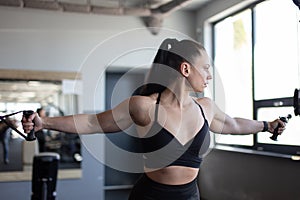 Fit young woman doing cable pec fly exercise in gym looking side grabbing handles