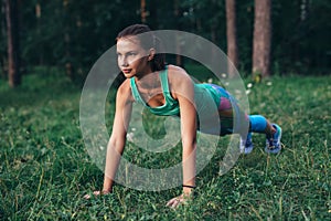 Fit young woman doing push-up exercise on grass in forest