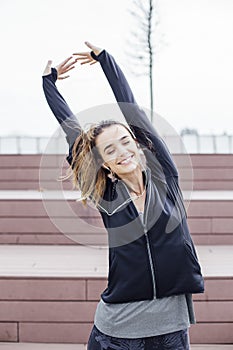 Fit young woman with earphones doing stretching exercises on stairs outdoors