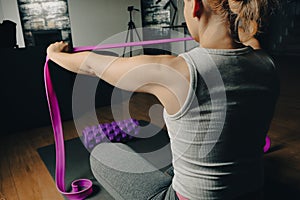 Fit young woman with exercise rubber bands for fitness and foam massage roller for myofascial release. Female athlete exercising