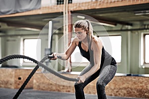 Fit young woman exercising with ropes at the gym