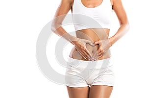 Fit young woman holding a heart over her abdomen, on white background