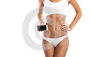 Fit young woman holding a smartphone over her abdomen, on white background