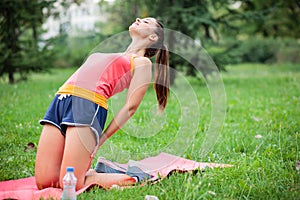 Fit young woman practicing yoga in a city park, doing Tibetan rite number three