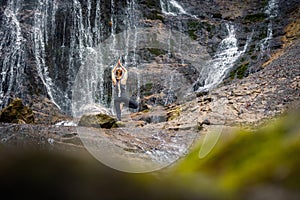 Fit young woman practicing yoga in waterfall scenery