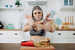 Fit young woman refusing junk food. Woman showing stop eating unhealthy food.