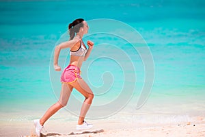 Fit young woman running along tropical beach in her sportswear