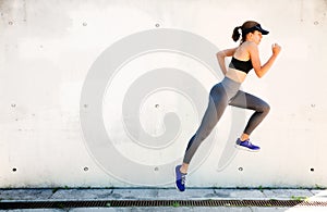 Fit young woman running and jumping with a white wall background