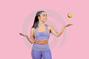 Fit young woman tossing apple on pink background