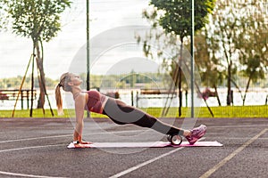 Fit young woman training on mat outdoor summer day, performing reverse plank with foam roller massager
