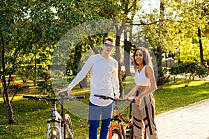 Fit, youthful and smiling couple is looking at the camera, cycling in the city park, laughing and spending their leisure on a