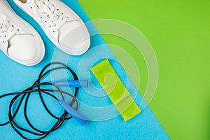Fitness accessories concept. Top view photo of a jump rope with elastic band and white sneakers on a two-tone green-blue