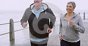 Fitness, active and healthy mature couple talking while running or jogging along a seaside promenade. Happy and sporty