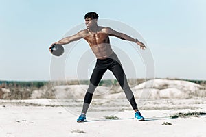 Fitness African American man doing workout twist exercise with medicine ball weight, outdoors on nature