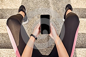 Fitness app. Top view of sporty woman hands holding black smartphone while sitting on stairs and resting after morning