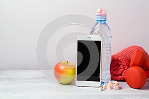Fitness background with bottle of water, dumbbells, apple and smartphone