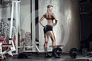 Fitness blonde girl prepares for exercising with barbell in gym