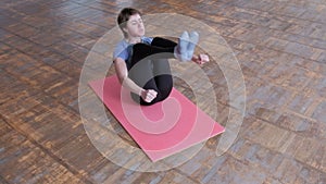 Fitness body flex. Exercise to strengthen the abdominal muscles. A woman athlete in a gray T-shirt and black tights lies on a pink