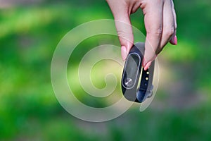 Fitness bracelet or smart watch on a woman`s hand. Against the background of green grass. Healthy lifestyle concept