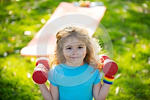 Fitness child boy raising a dumbbell. Cute child training with dumbbells. Children fitness. Kid boy exercising with