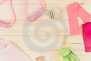 Fitness clothes and accessories for woman on wooden background. Sports fashion with t-shirt, elastic bands, headphones,