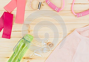 Fitness clothes and accessories for woman on wooden background. Sports fashion with t-shirt, elastic bands, headphones,