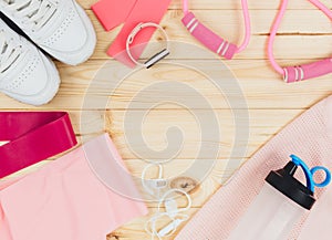 Fitness clothes and accessories for woman on wooden background. Sports fashion with t-shirt, elastic bands, headphones, sneakers,