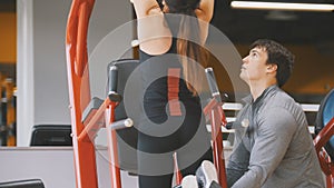 Fitness-club - young woman performs Pull-Ups with male coach - rear view, close up