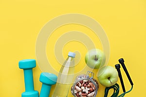 Fitness concept - apples, water, nuts, dumbbells and skipping rope on yellow background. Place for your text.