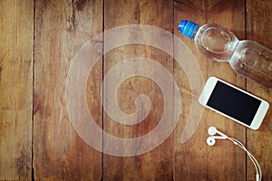 Fitness concept with bottle of water, mobile phone with earphones over wooden background. filtered image