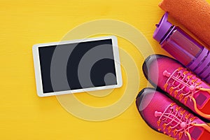 fitness concept with bottle of water, towel, tablet devise and woman pink sport footwear over colorful background