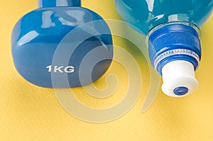 Fitness concept with dumbbell and bottle/blue dumbbell and bottle on a yellow background. Top view