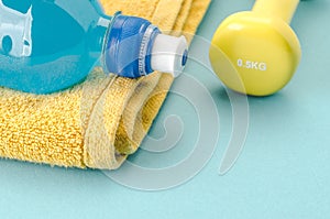 Fitness concept with dumbbell, towel and bottle/yellow dumbbell, towel and bottle on a blue background. selective focus