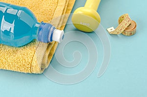 Fitness concept with dumbbell, towel, measure tape and bottle/yellow dumbbell, towel, measure tape and bottle on a blue