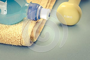 Fitness concept with dumbbell, towel, measure tape and bottle/yellow dumbbell, towel, measure tape and bottle on a blue background