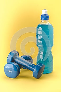 Fitness concept with dumbbells and bottle/blue dumbbells and bottle on a yellow background