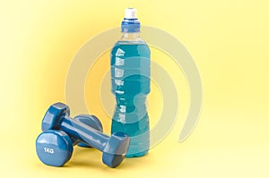 Fitness concept with dumbbells and bottle/blue dumbbells and bottle on a yellow background. Copy space