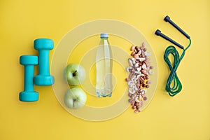 Fitness concept with dumbbells, nuts, water, bananas, apples and skipping rope on color background.