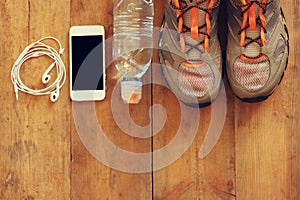 Fitness concept with mobile phone with earphones, towel and sport footwear over wooden background