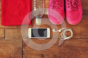 Fitness concept with mobile phone with towel and woman sport footwear over wooden background.