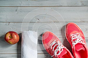 Fitness concept, pink sneakers, red apple and white towel on wooden background, top view