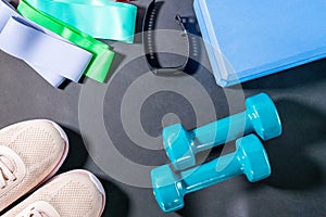 Fitness concept with sneakers, dumbbells, fitness bracelet, tracker, elastic expanders. Sports equipment on a black background.