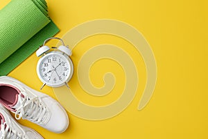 Fitness concept. Top view photo of white sneakers green sports mat and alarm clock on isolated yellow background with copyspace