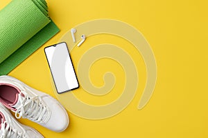 Fitness concept. Top view photo of white sneakers green sports mat smartphone and earbuds on isolated yellow background with