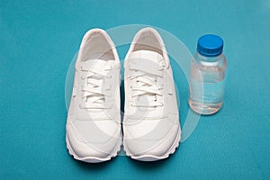 Fitness concept with white sneakers and a water bottle. Top view on a blue background. Copy space