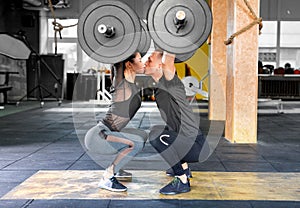 Fitness couple making a Barbell Jerk and kissing each other. Sporty family in gym.